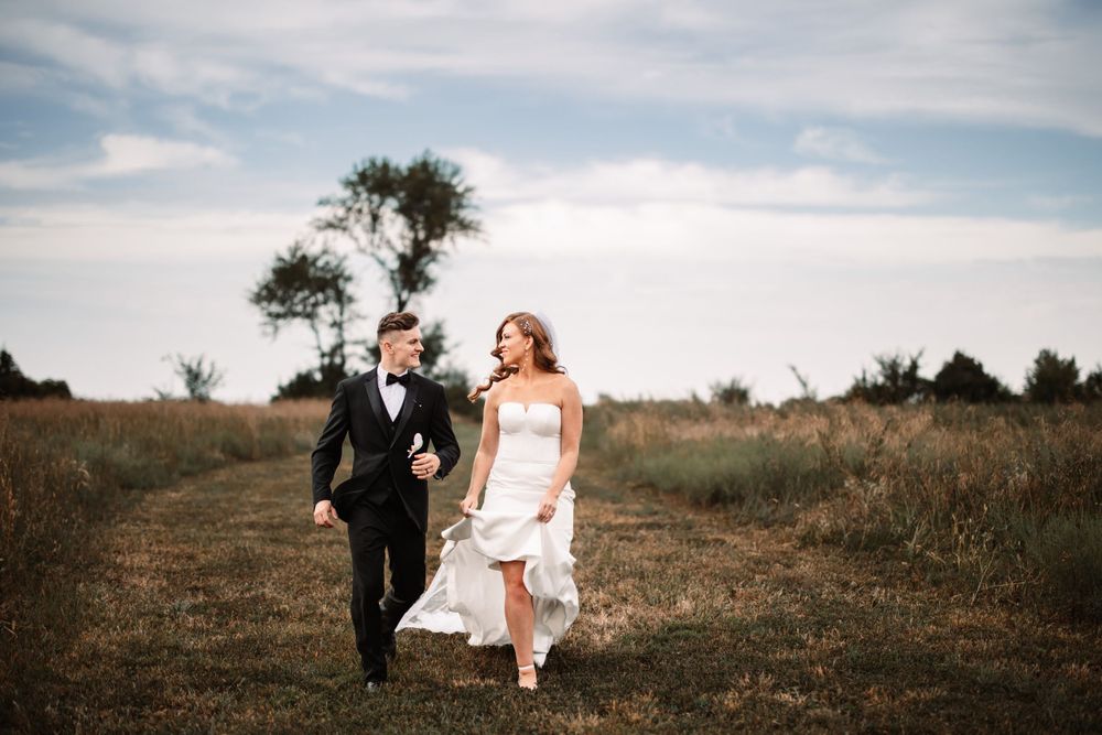 Couple runs joyfully through meadow during countryside wedding photoshoot.