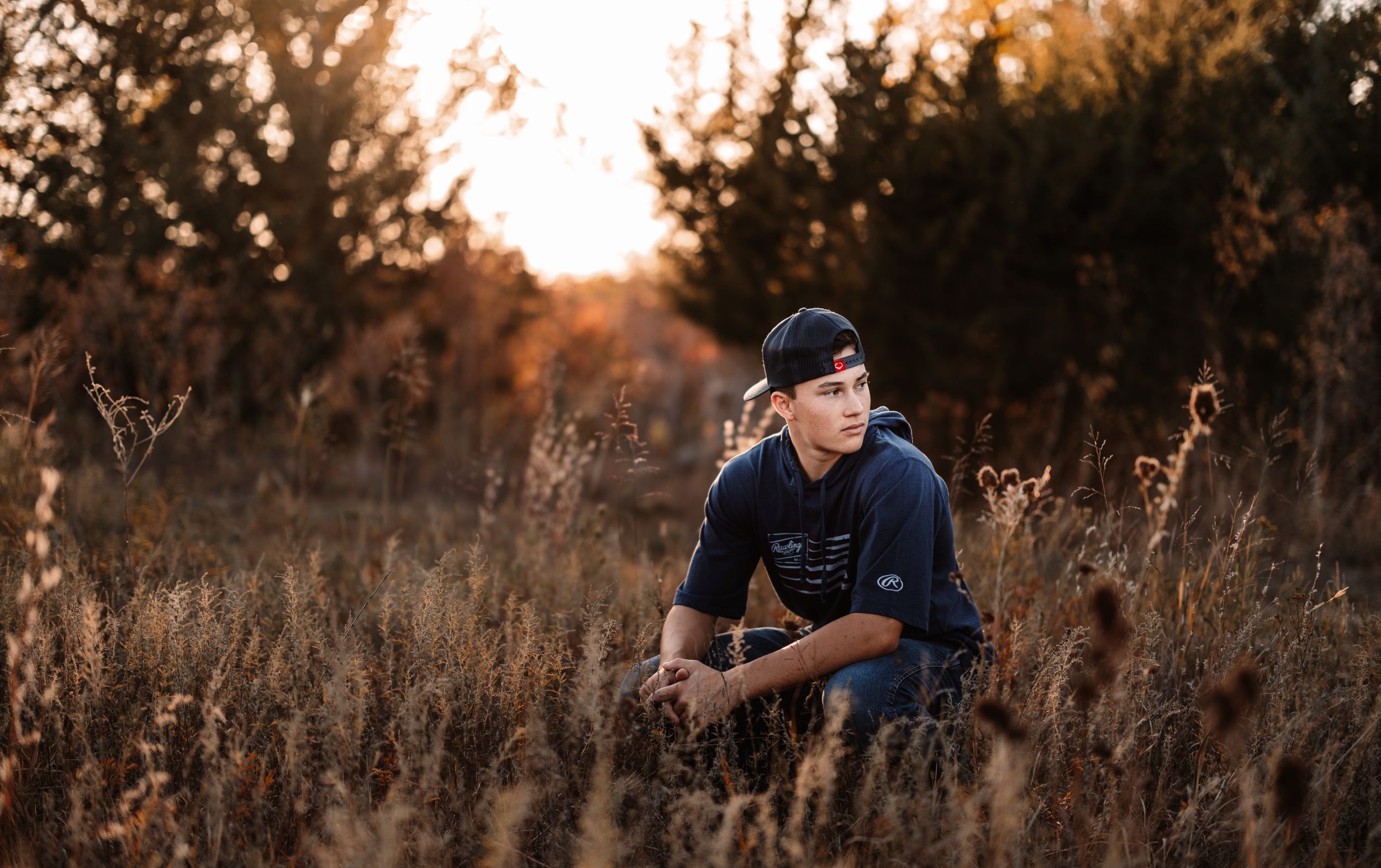 Portrait of person in navy hoodie sitting in golden autumn field during sunset.