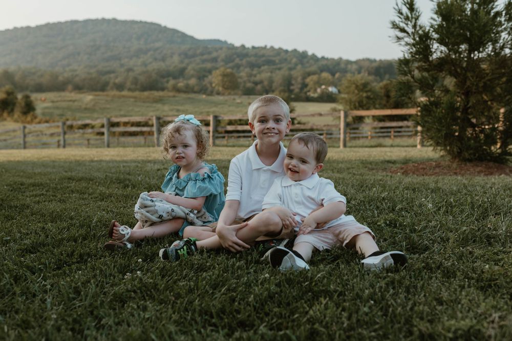 Children relaxing together on grass with mountain scenery in background.