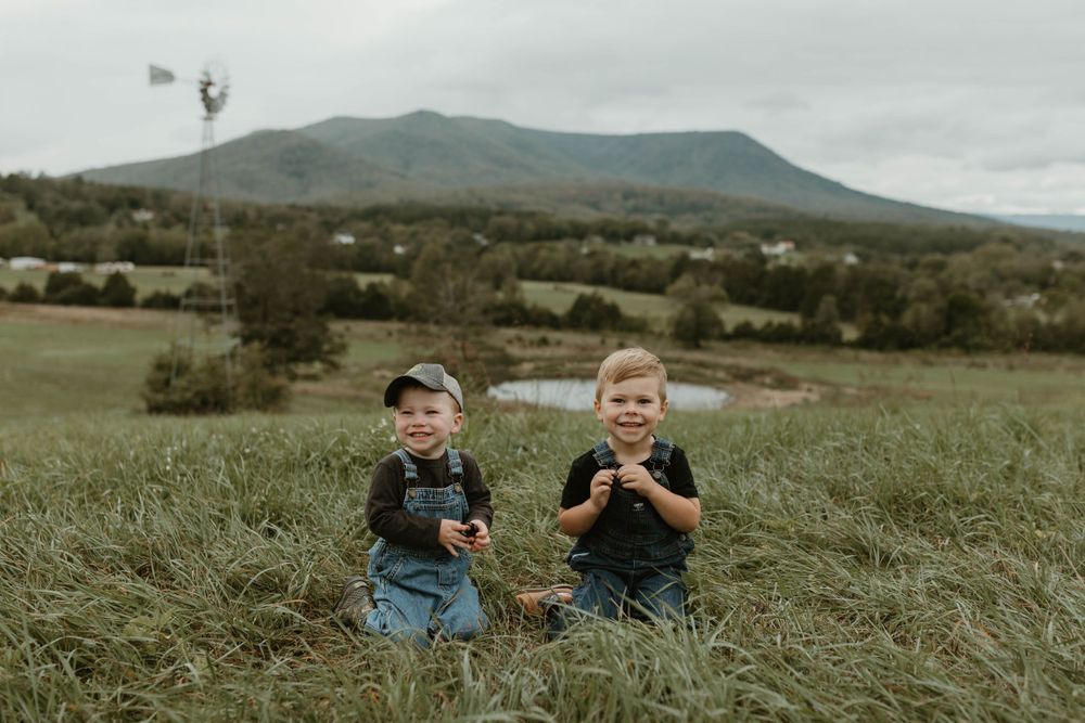 Children sitting together in tall grass with mountains visible in overcast background.