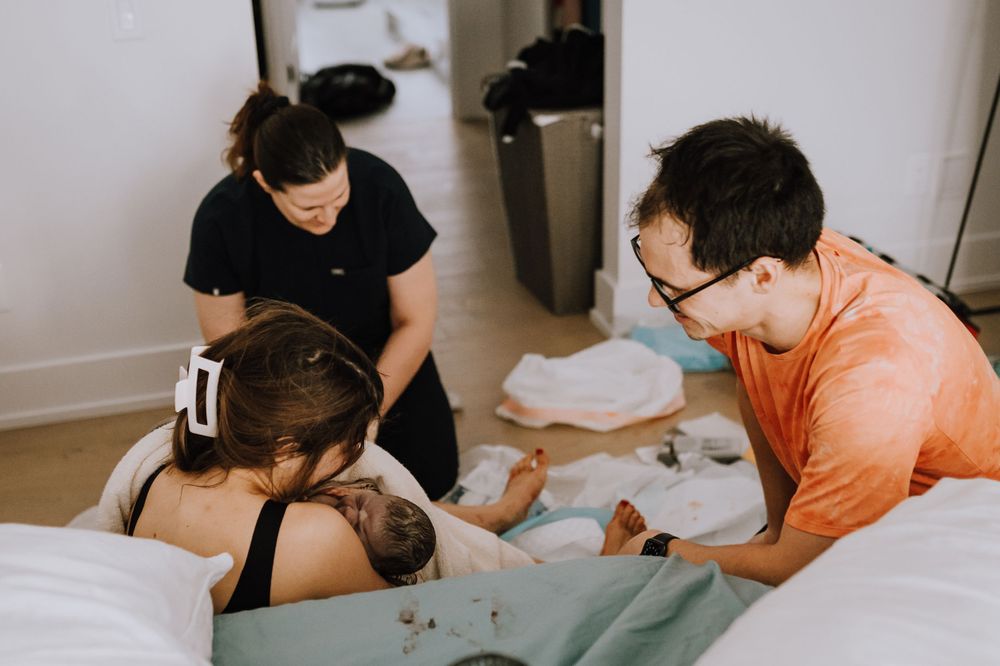 Support team provides comfort and care during home birth with birthing pool in the background.