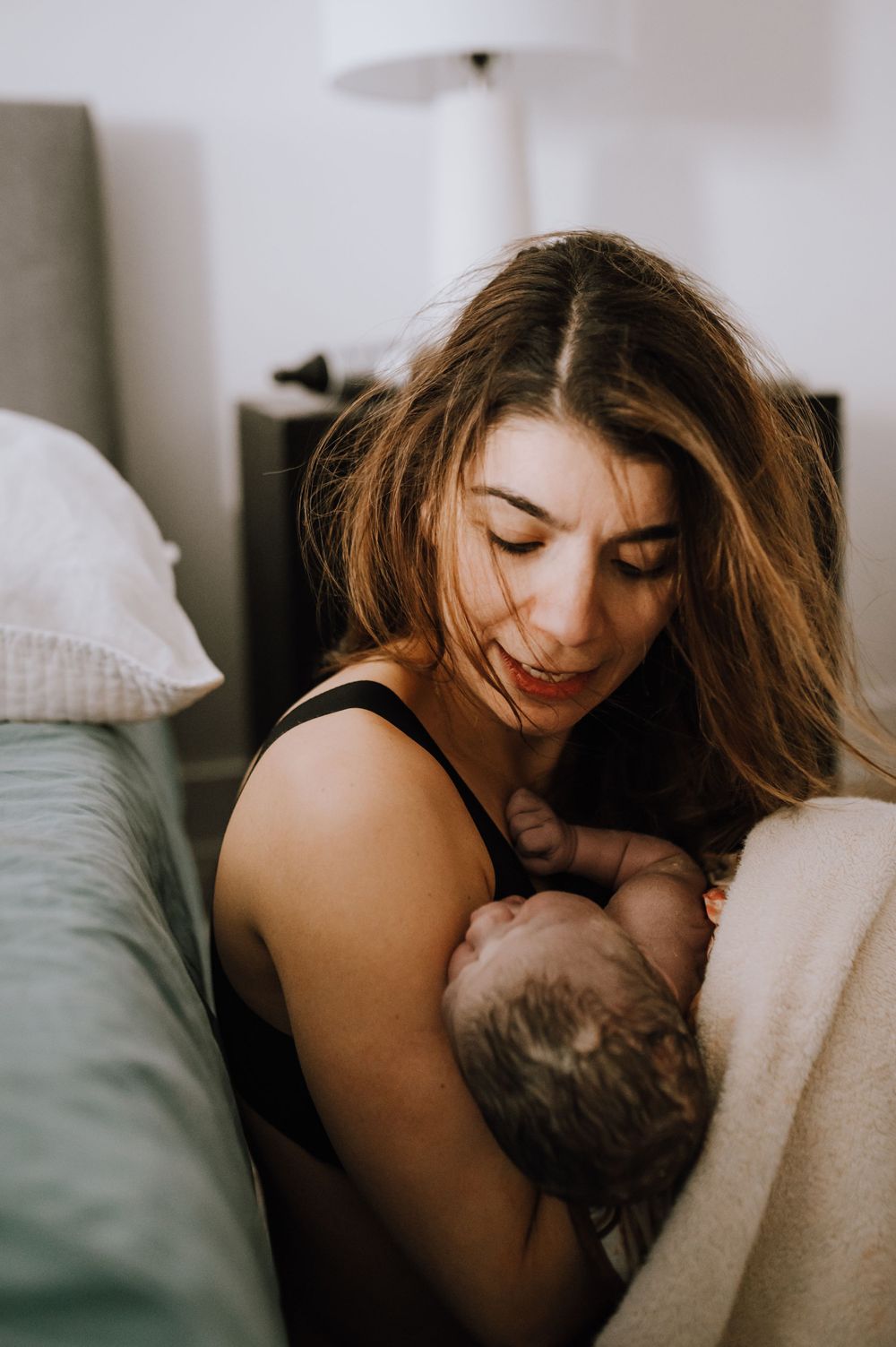 A tender moment between mother and baby as they share an intimate embrace in bed with soft natural lighting.