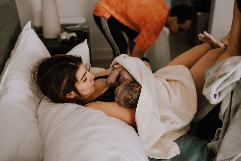 Someone resting on white bedding while cuddling with a small pet dog.