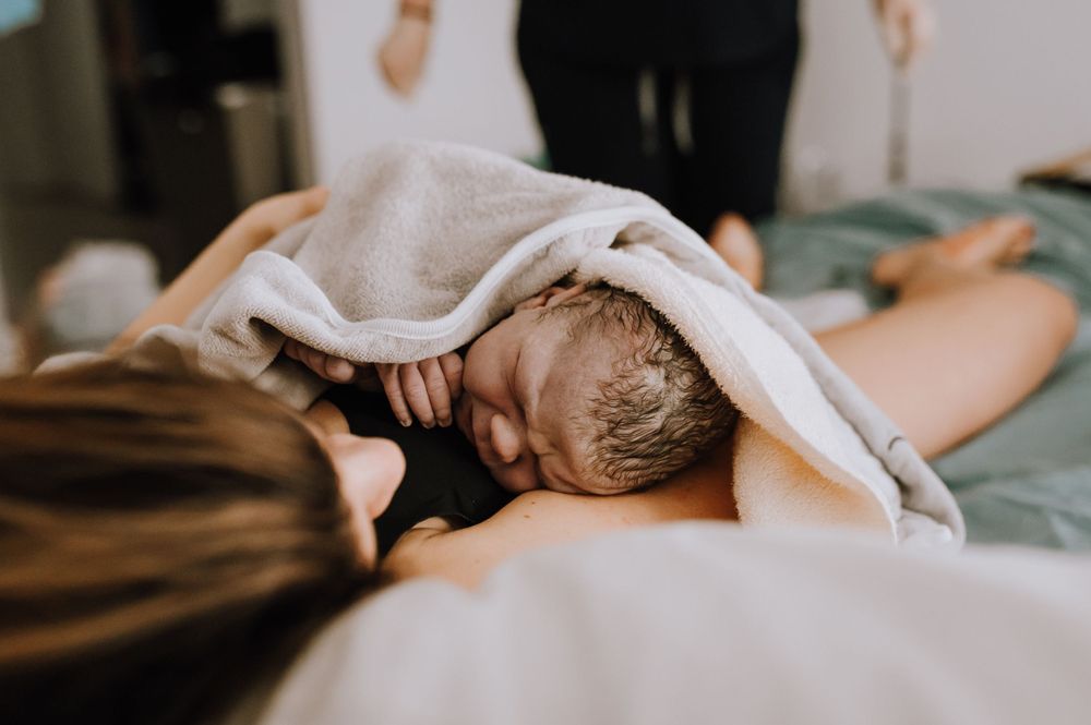 Newborn baby wrapped in soft white towel during home birth.