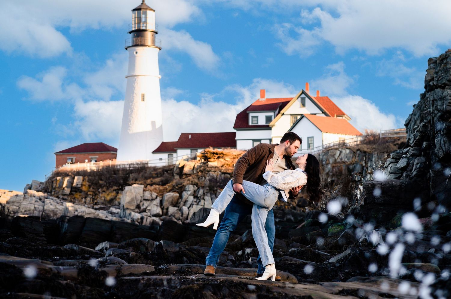 Snowy lighthouse scene with white buildings against bright blue winter sky.