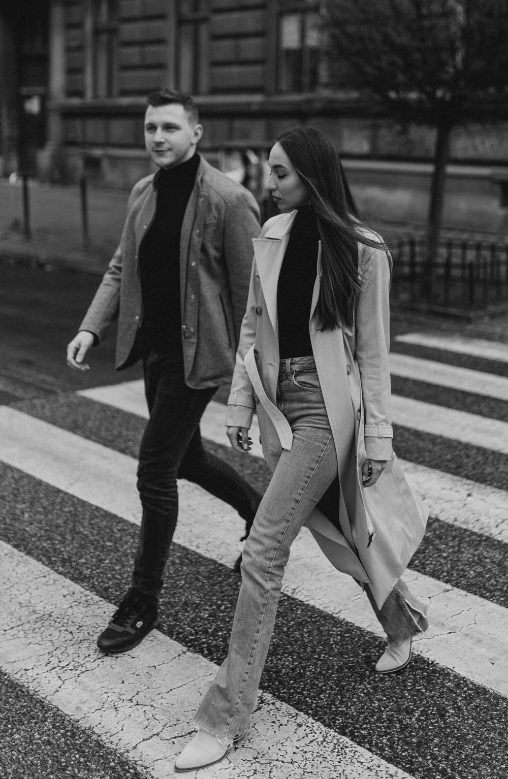 Stylish couple walking across crosswalk in matching black and beige winter outfits.
