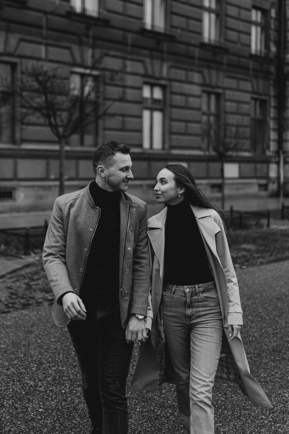 Candid black and white shot of couple walking together in winter coats near historic building.