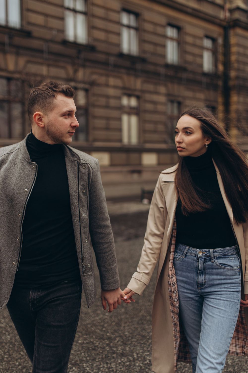 Couple in matching turtlenecks and long coats holding hands while walking outdoors.