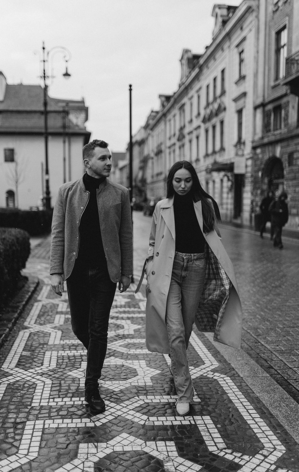 A stylish couple walking together on a patterned cobblestone street in European city.