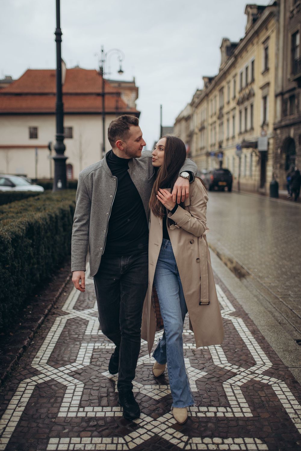 A couple in winter coats sharing a tender moment while walking down a historic street.