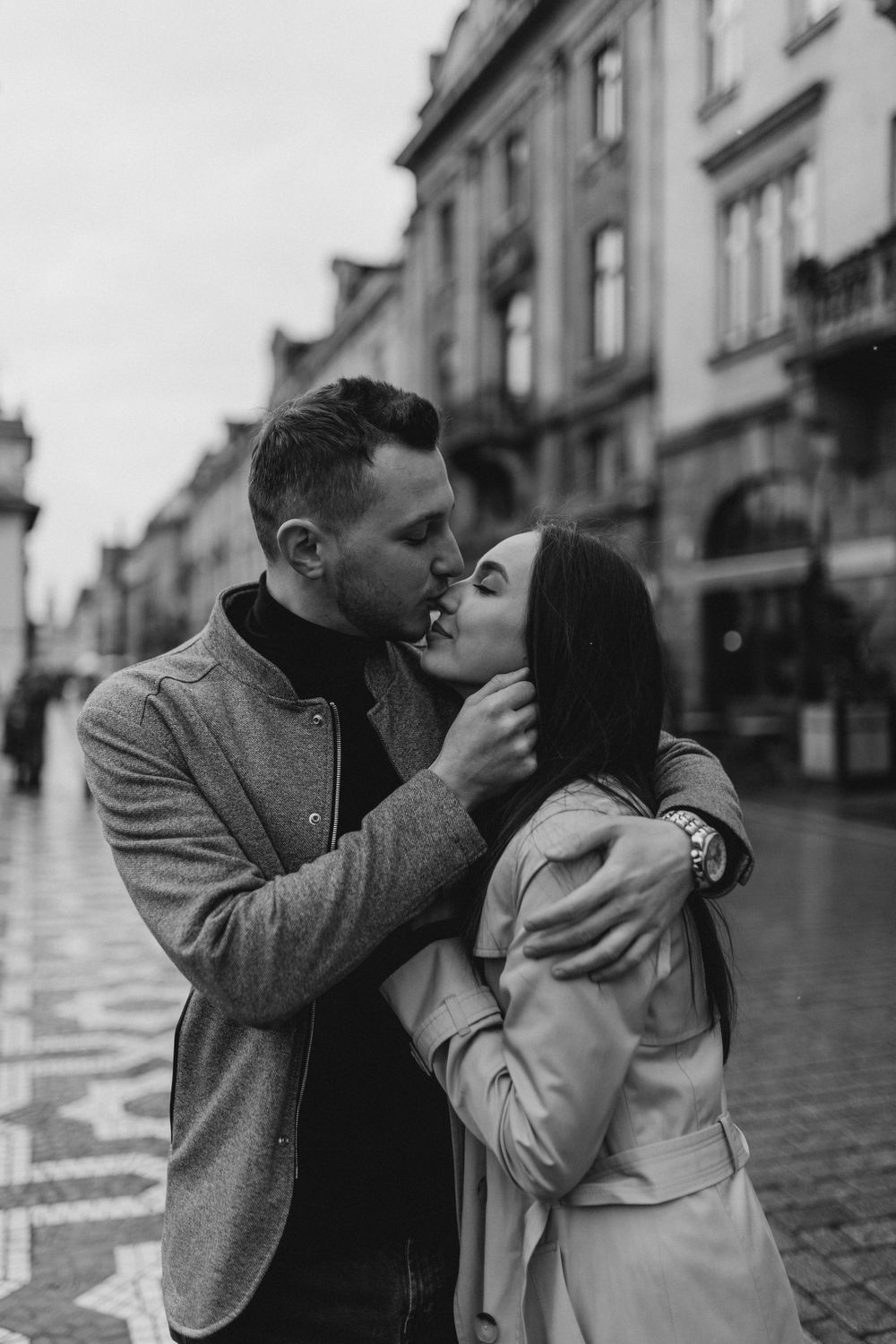 A couple sharing a passionate kiss on a rainy European street corner.