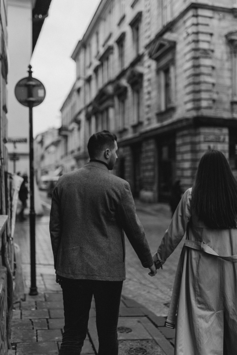 A couple holding hands while walking down a historic street with vintage architecture.