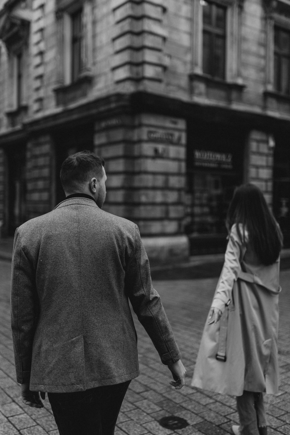 A couple walking together on a cloudy day in front of historic European architecture.
