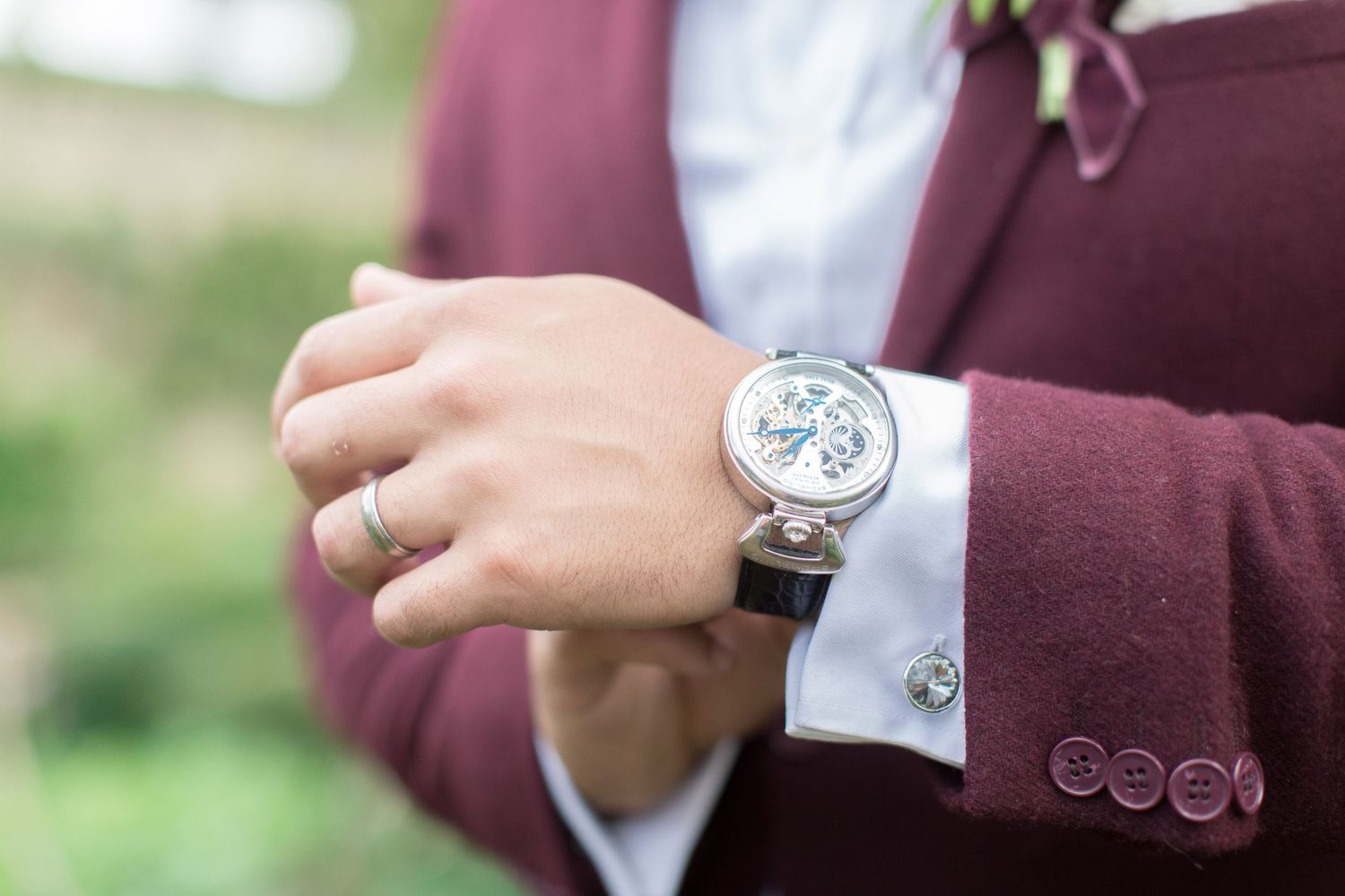 A close-up shot of a white chronograph watch and suit sleeve cuff in burgundy, with a wedding ring visible euridge manor