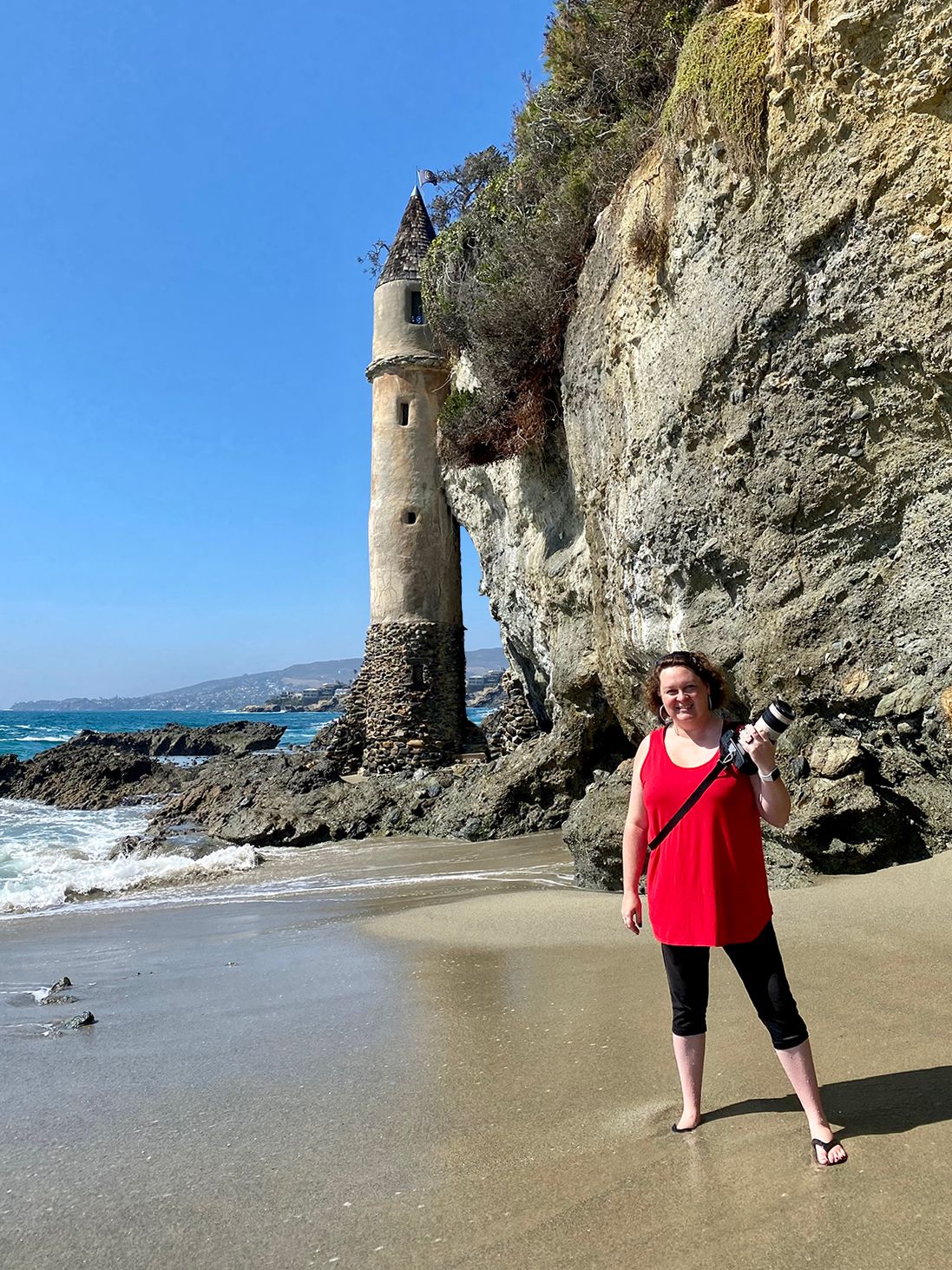 Leslie Sessums, photographer with camera in hand, in front of Victoria Beach Pirate Tower in Laguna Beach, California on a sunny day