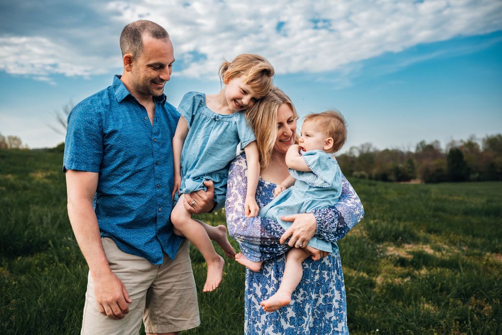 A family walks together through a grassy field under bright blue summer skies.