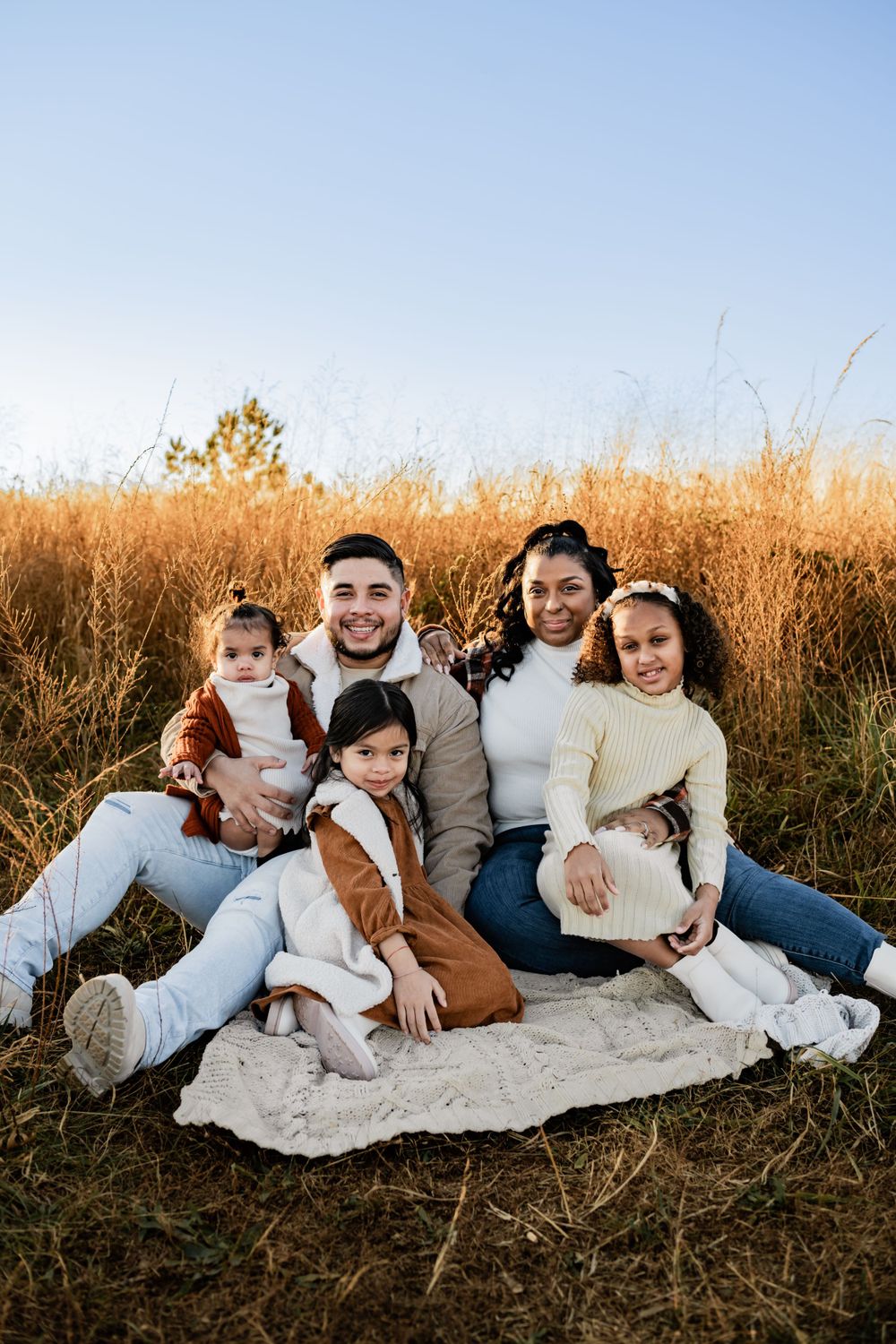 A family sits together on a blanket in a golden field of tall grass during sunset.