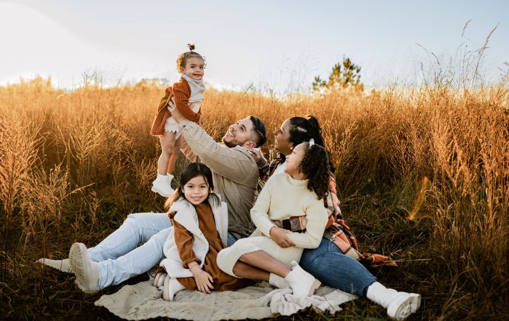 A candid family moment captured in a sun-lit field with tall golden grass.