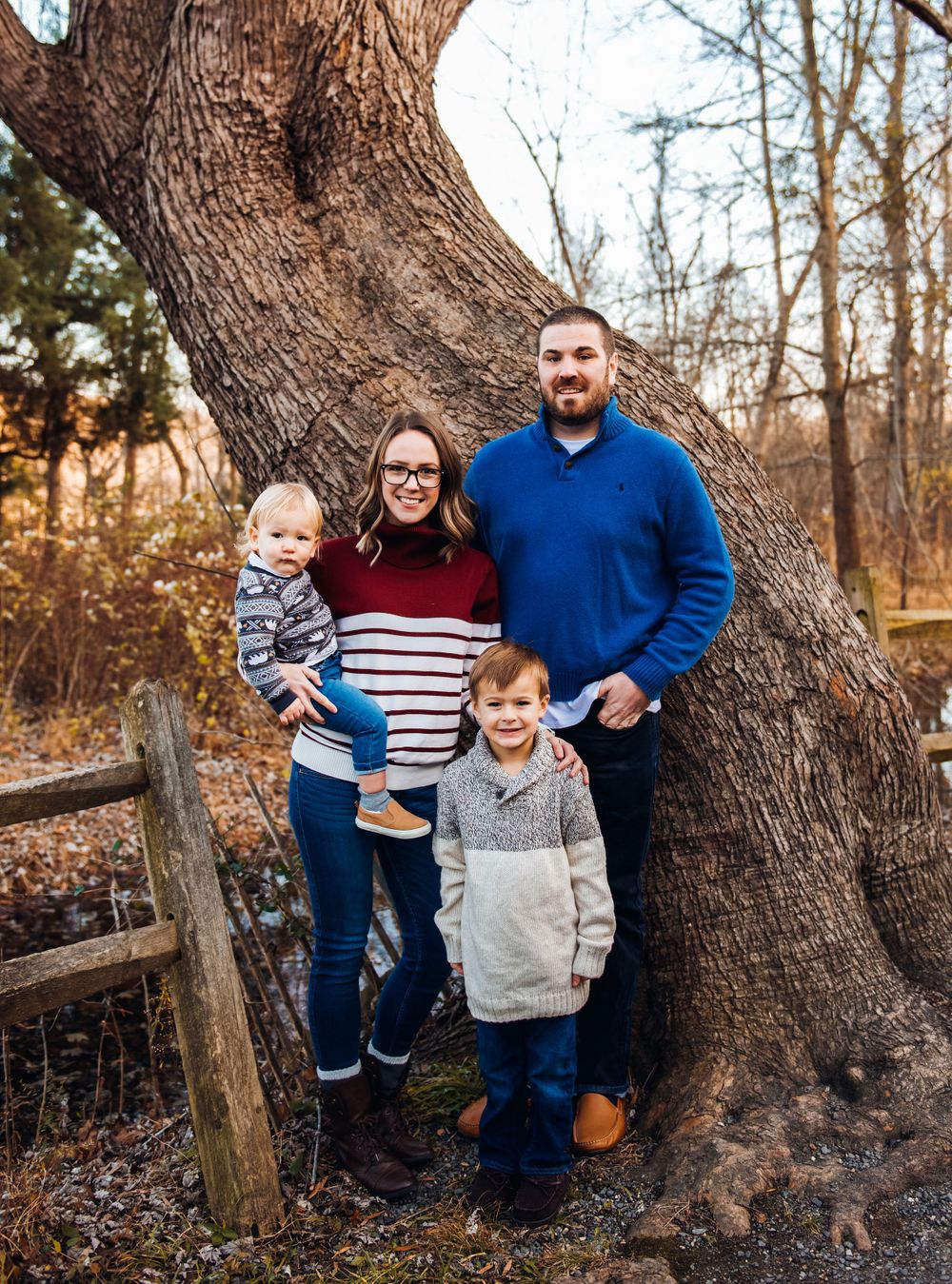Family posing together near large tree trunk during fall photo session.