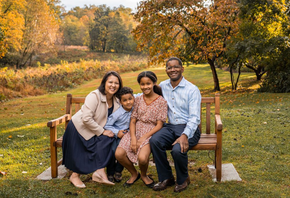 A family sits together on a wooden bench against a stunning autumn backdrop with golden foliage.