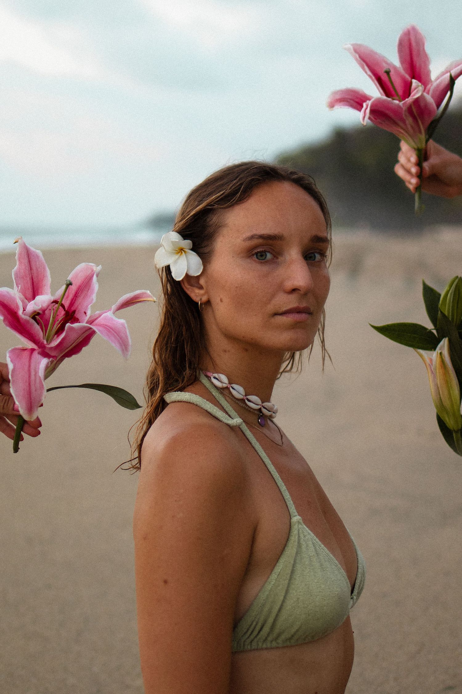 A dreamy beach portrait with pink lilies and a white plumeria flower against a coastal backdrop.