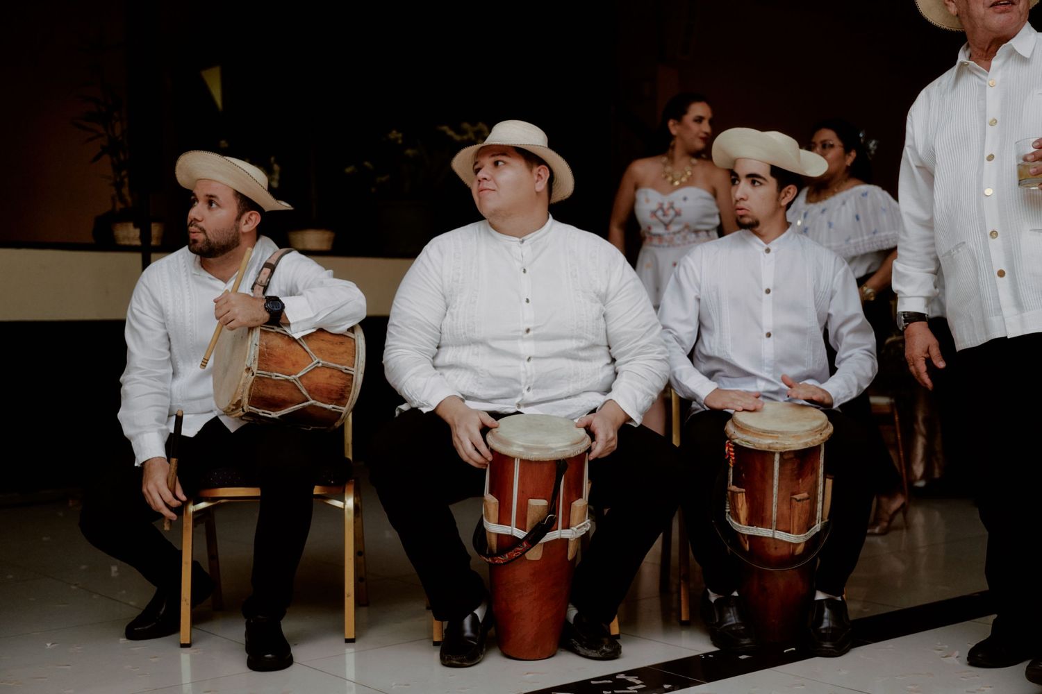 Musicians in white shirts playing traditional drums during a cultural performance.