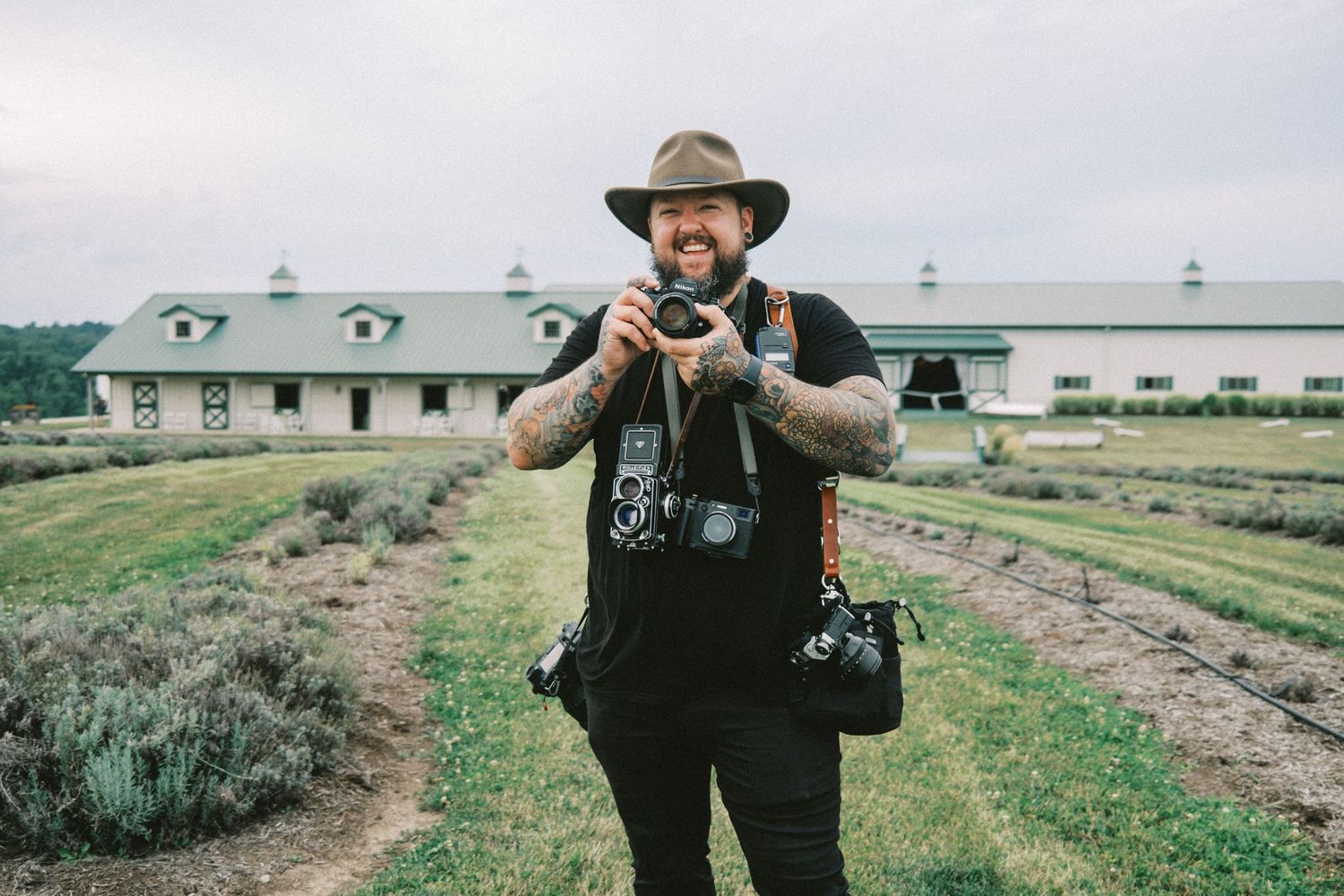 Photographer wearing a cowboy hat taking photos in a rural field setting.