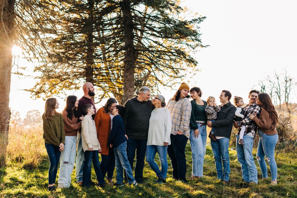 A large group poses together outdoors during golden hour under a tall tree.