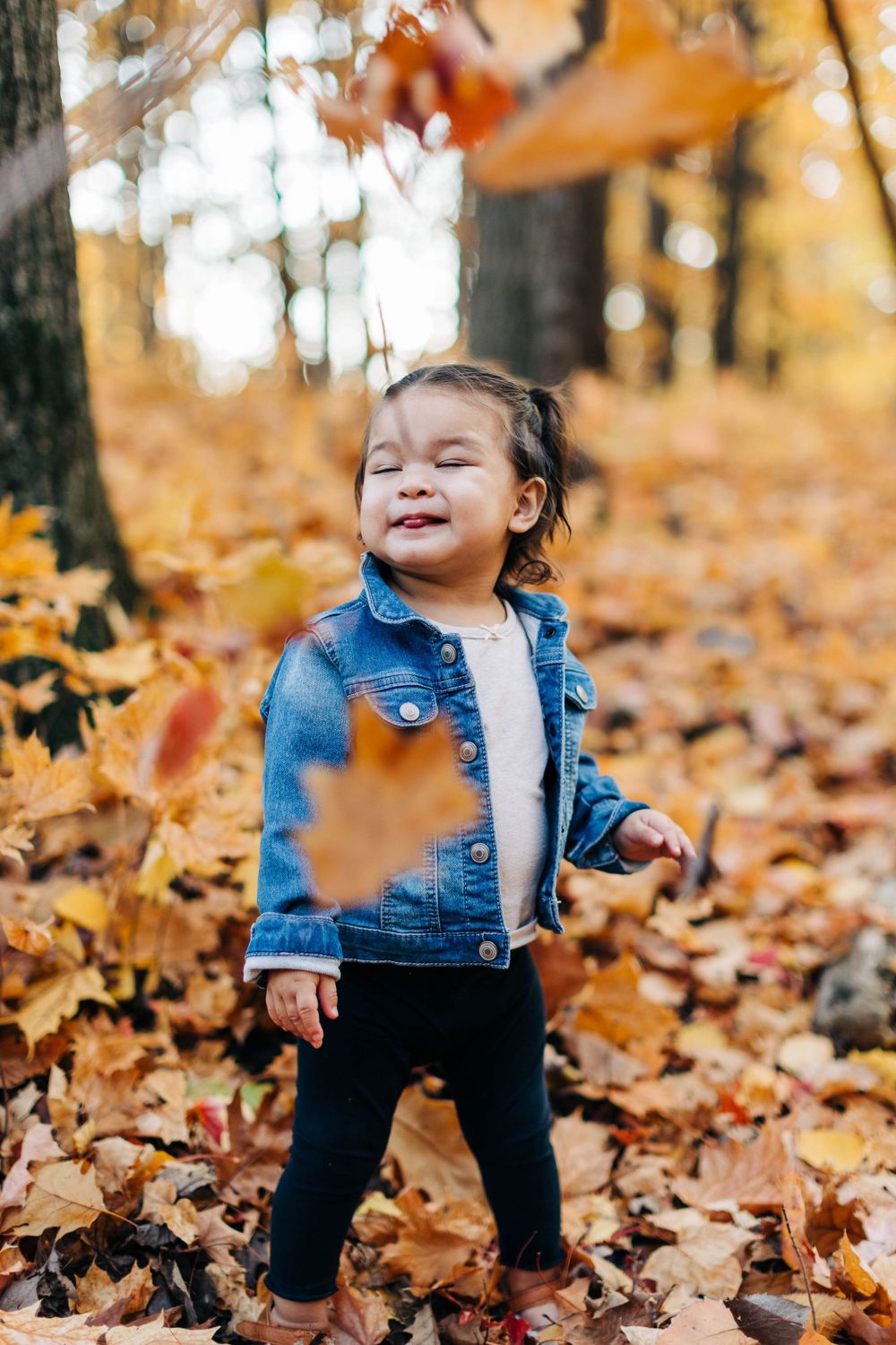Child in denim jacket plays with falling autumn leaves.
