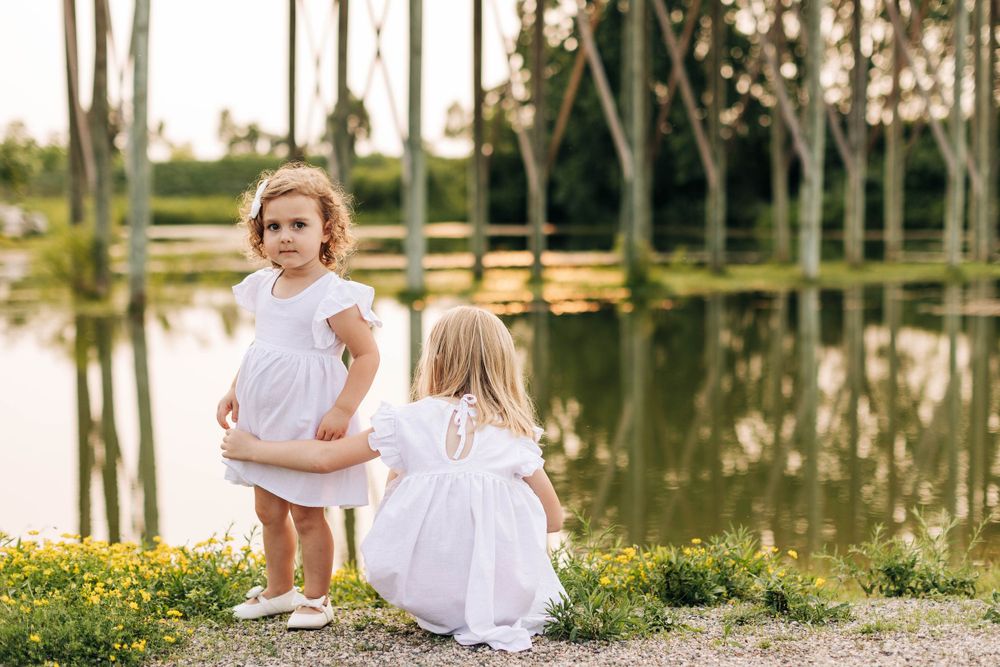 Two children in white dresses playing near a reflective pond with palm trees.