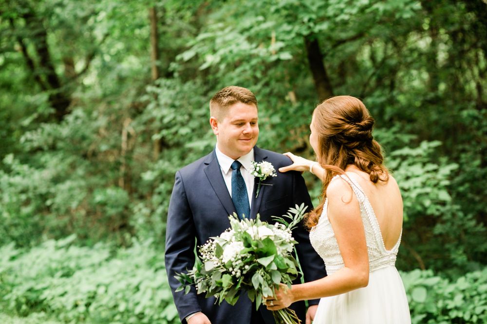 Groom smiling as bride taps his shoulder during outdoor first look reveal.