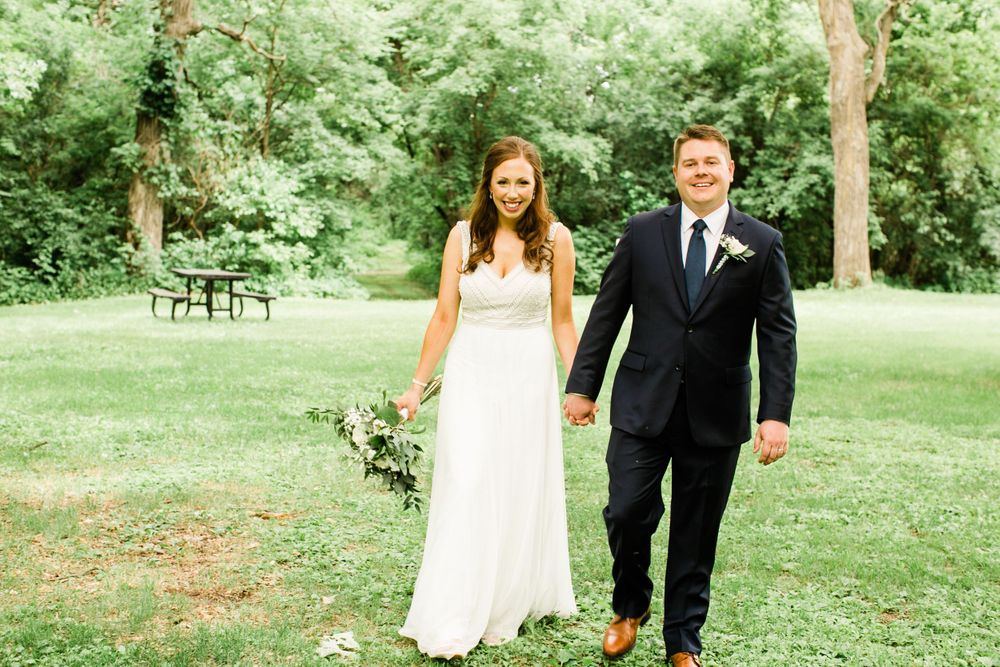 Bride and groom walking hand in hand across a green lawn on their wedding day.