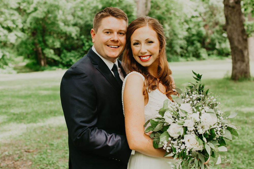 Happy bride and groom smiling closely together outdoors with a white floral bouquet.
