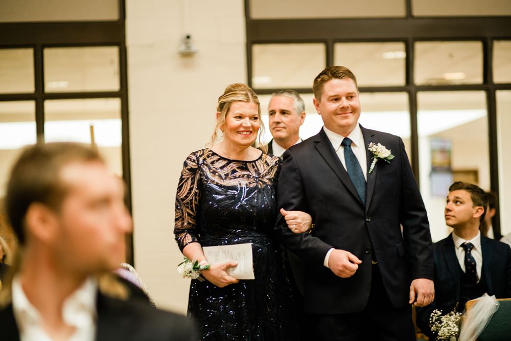 Groom walking down the aisle with a woman in a navy lace dress during wedding ceremony.