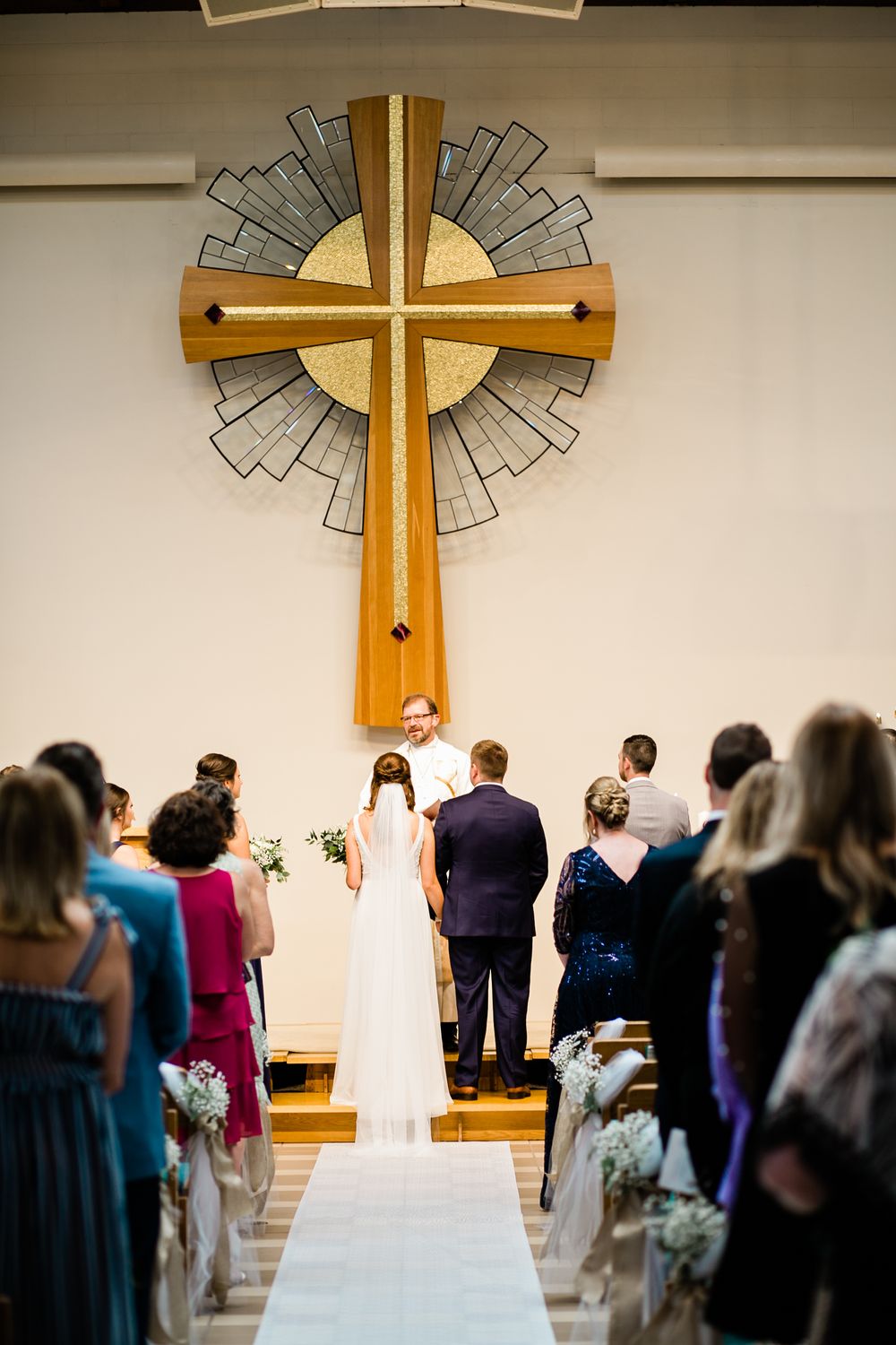 Bride and groom stand at church altar beneath large wooden cross during Christian wedding ceremony.