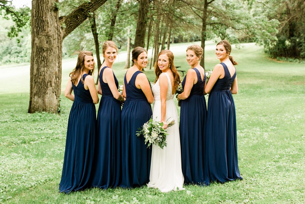 Bride in white gown and bridesmaids in navy dresses pose with backs turned, showing elegant dress details.