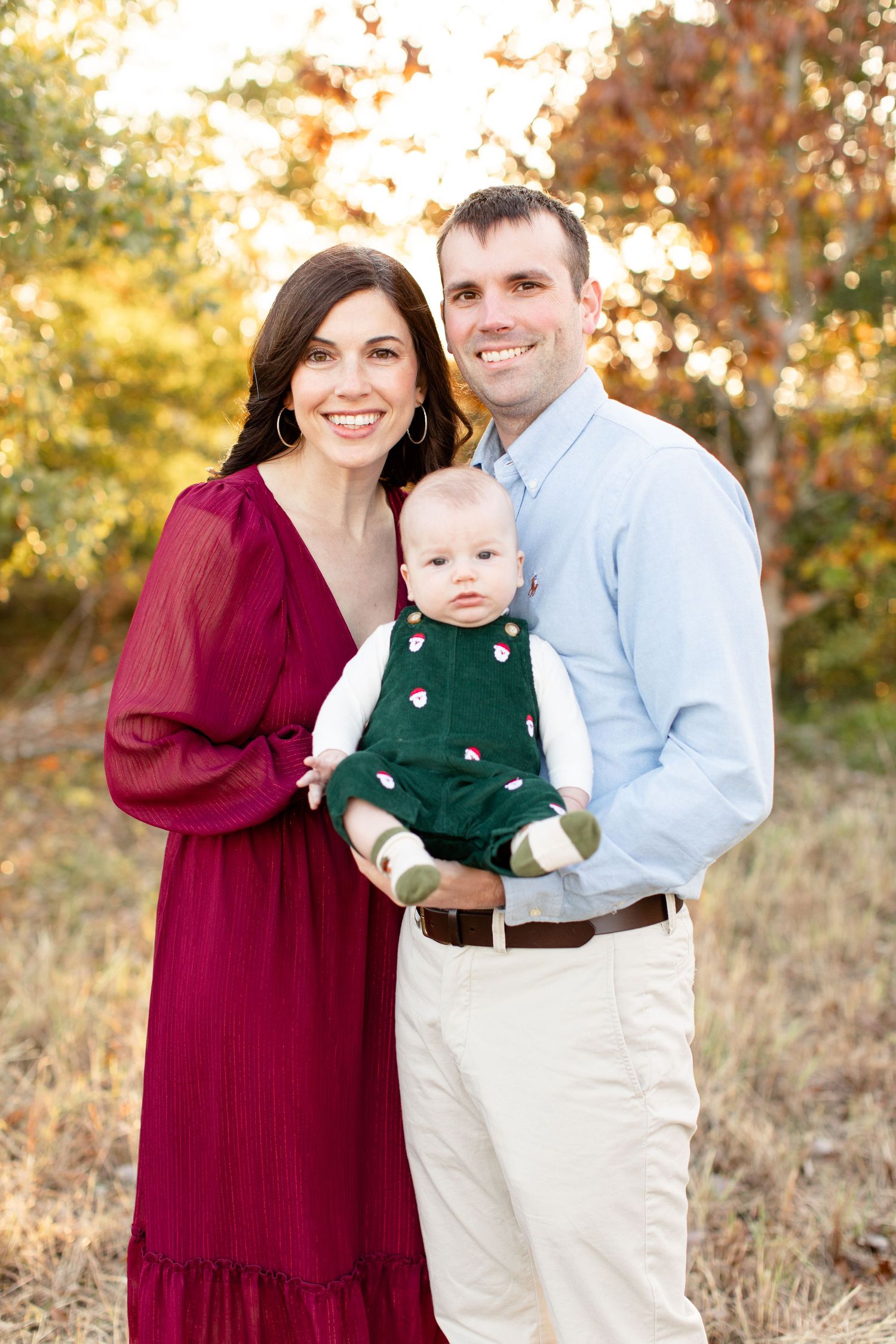 Joyful outdoor family photo with burgundy dress and casual attire against autumn trees.