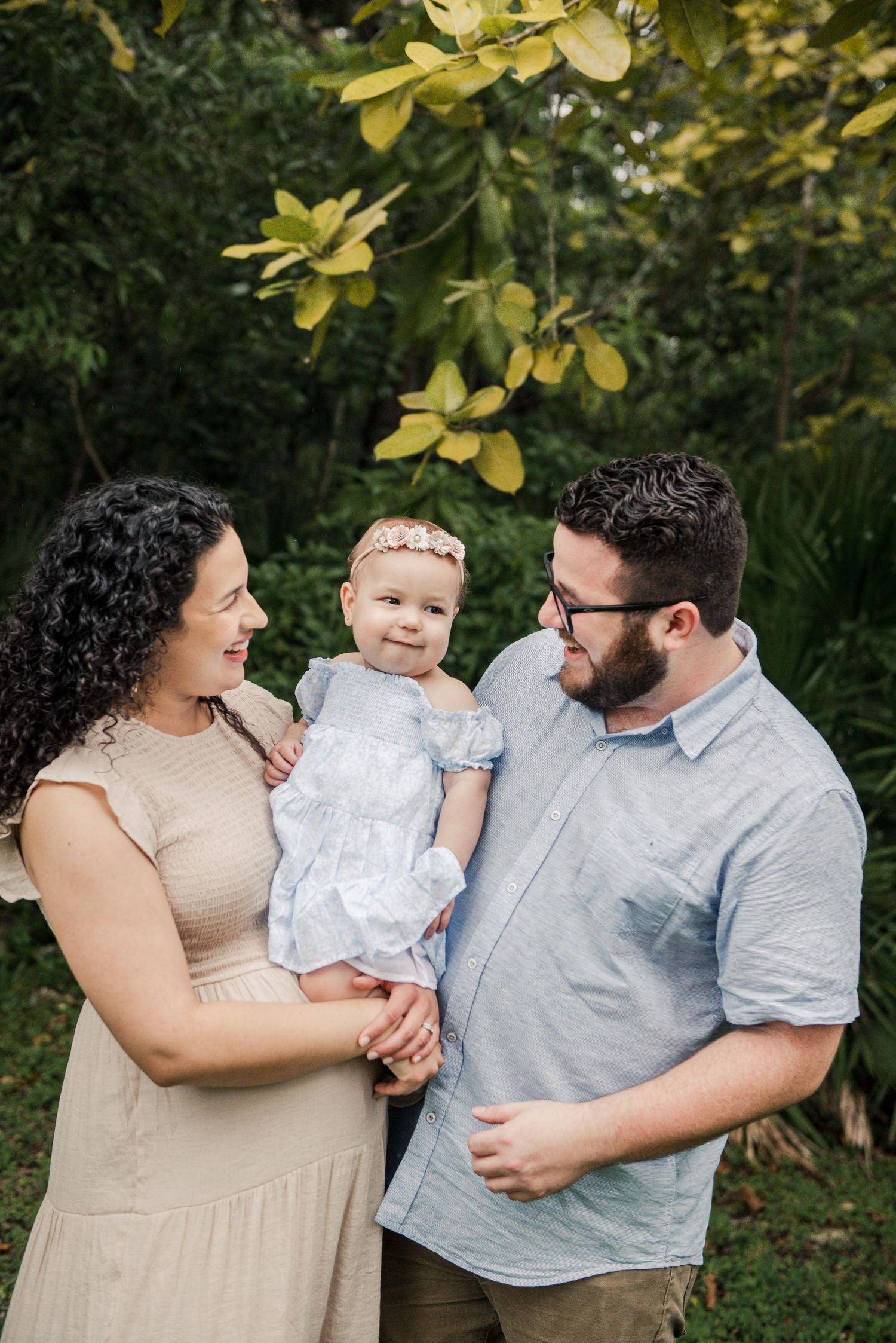 Family of three poses together in lush garden setting.