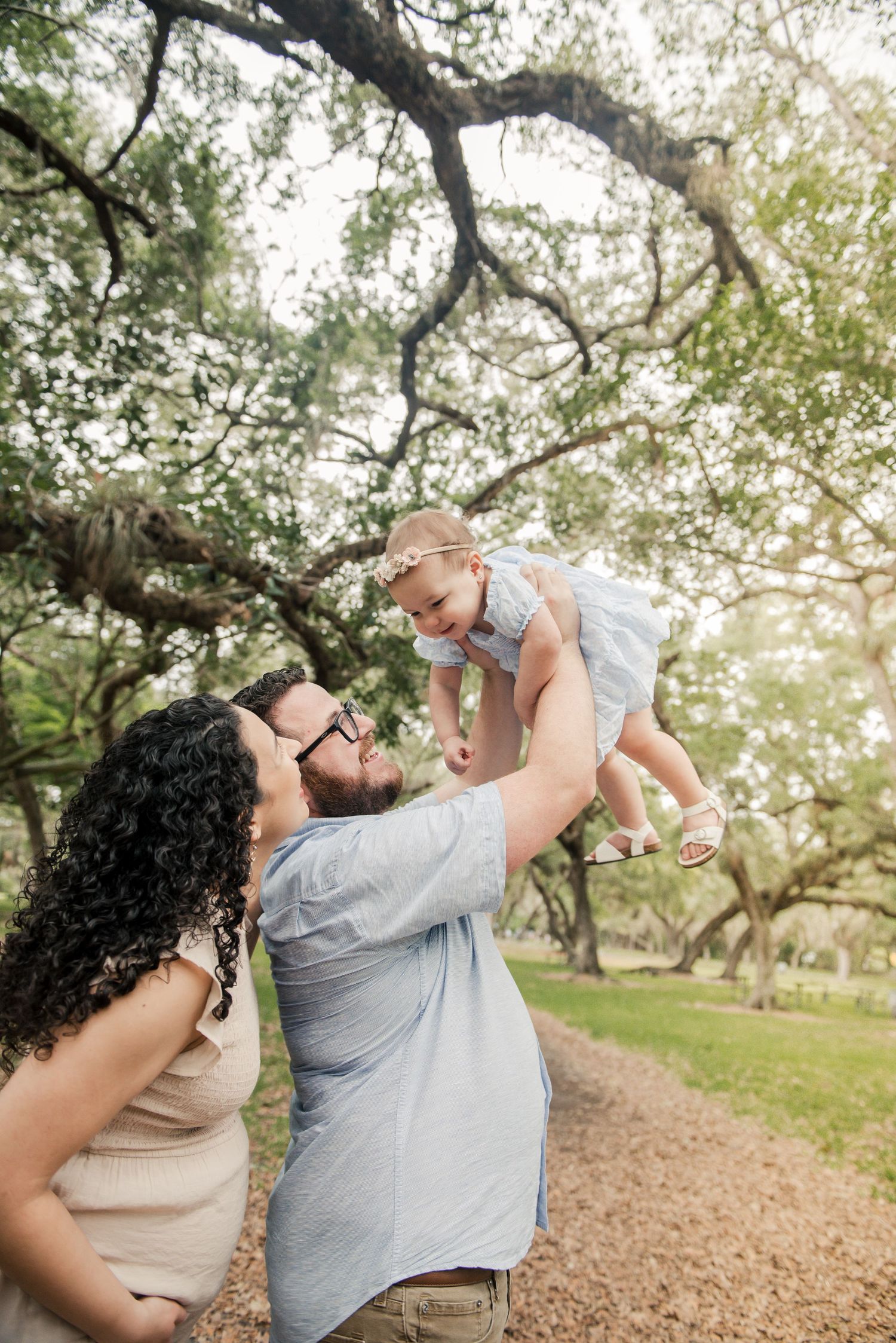 A family shares a tender outdoor moment together on a dirt path under sprawling oak tree branches.