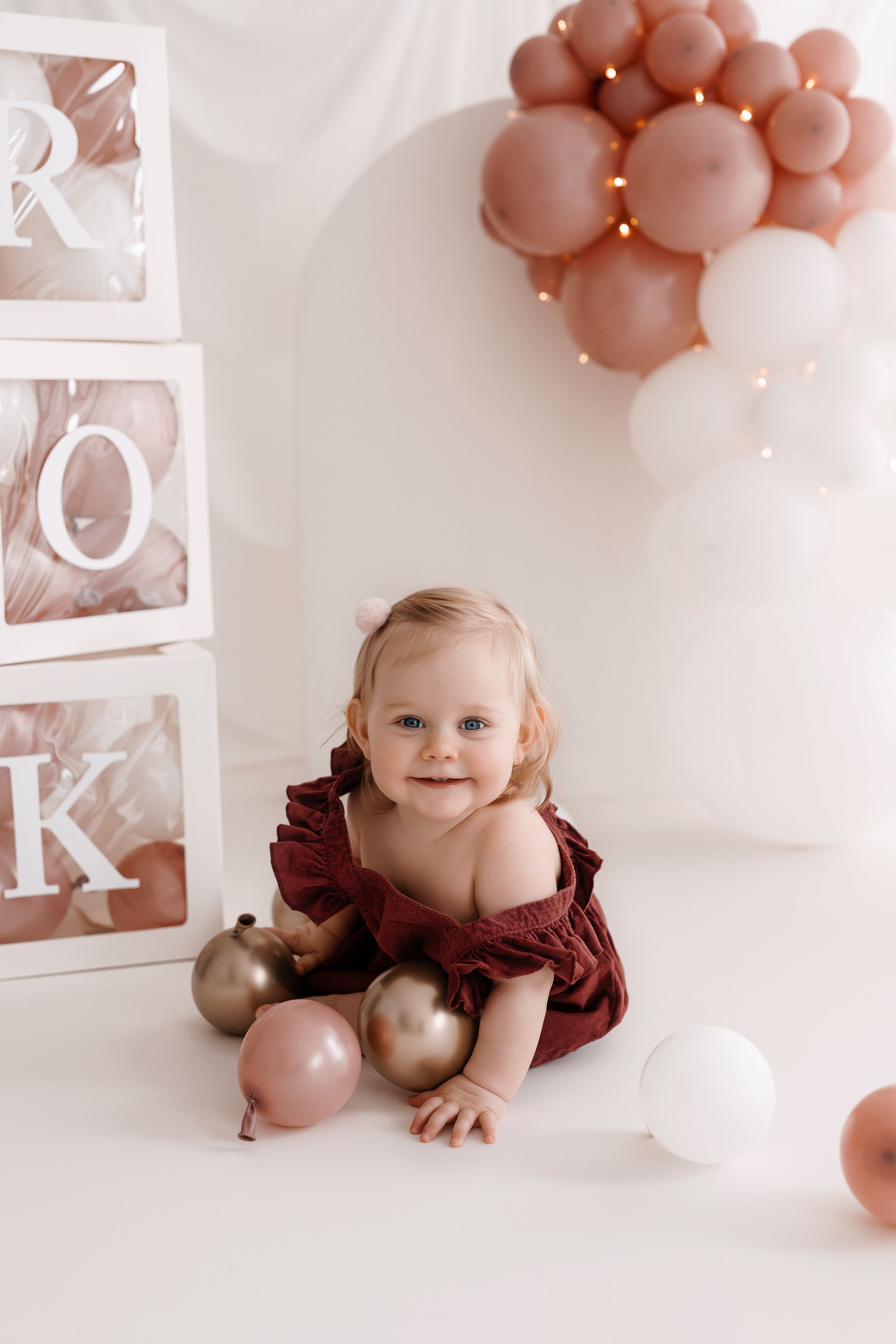 Studio photo setup with balloon arch and decorative blocks in soft pink tones.