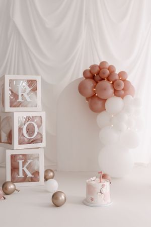 Minimalist birthday setup with ROK blocks, rose gold balloons, and a small cake on white background.