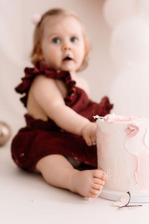 Soft focus photo of toddler in burgundy dress reaching for birthday cake.