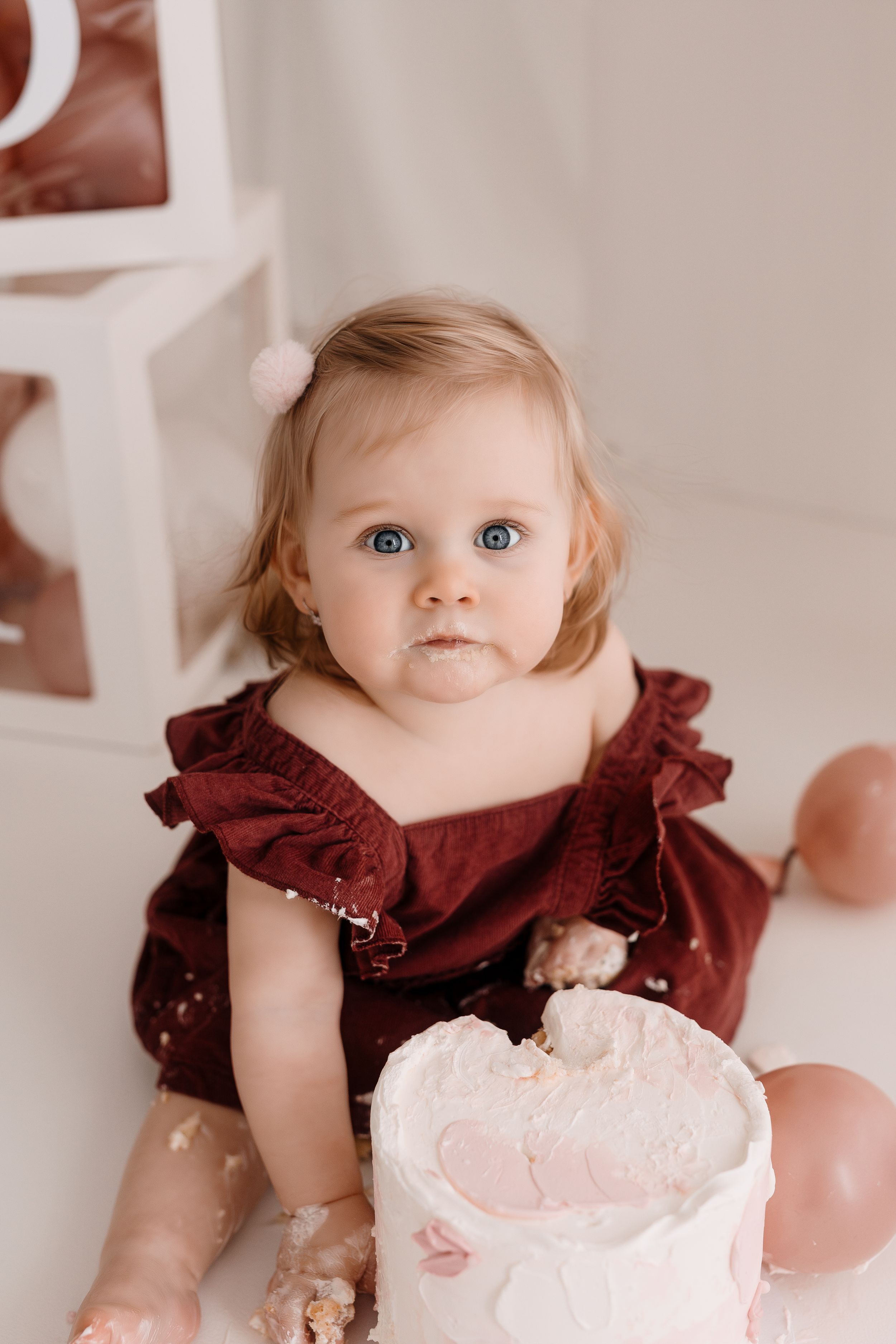 A close-up shot of a toddler in burgundy dress with a birthday cake.