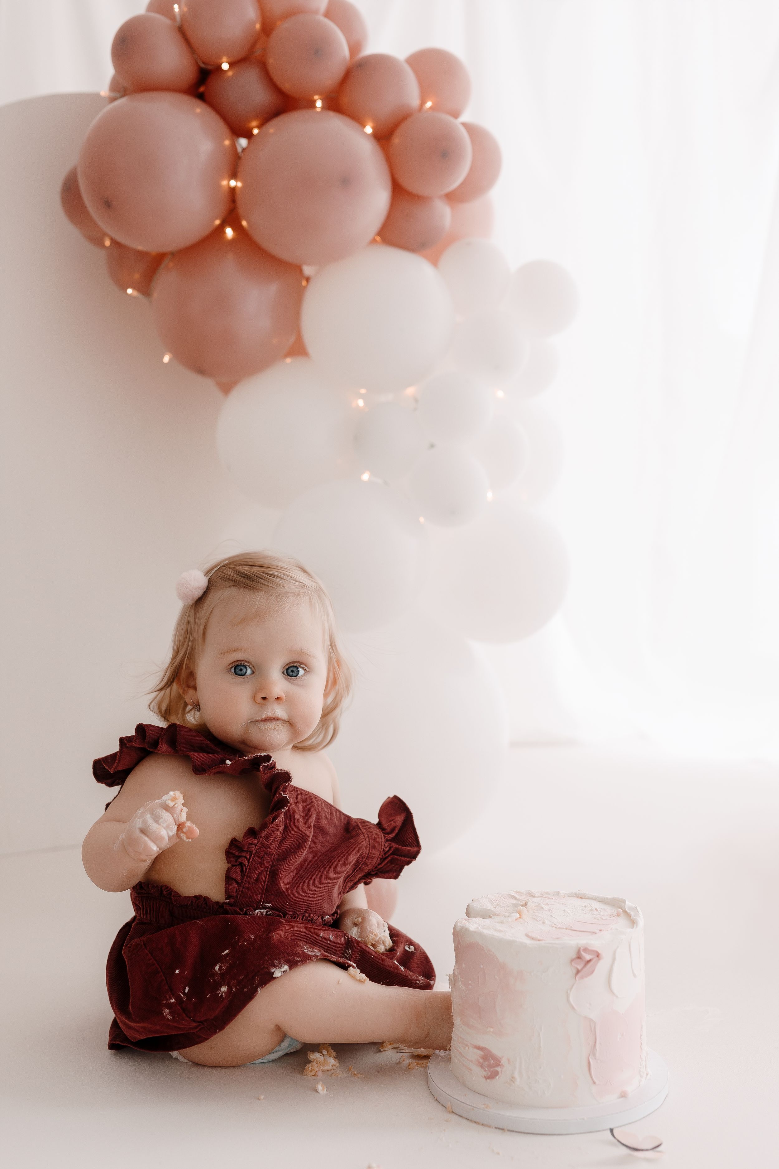 Studio birthday photo with rose gold balloon arrangement and small white cake.