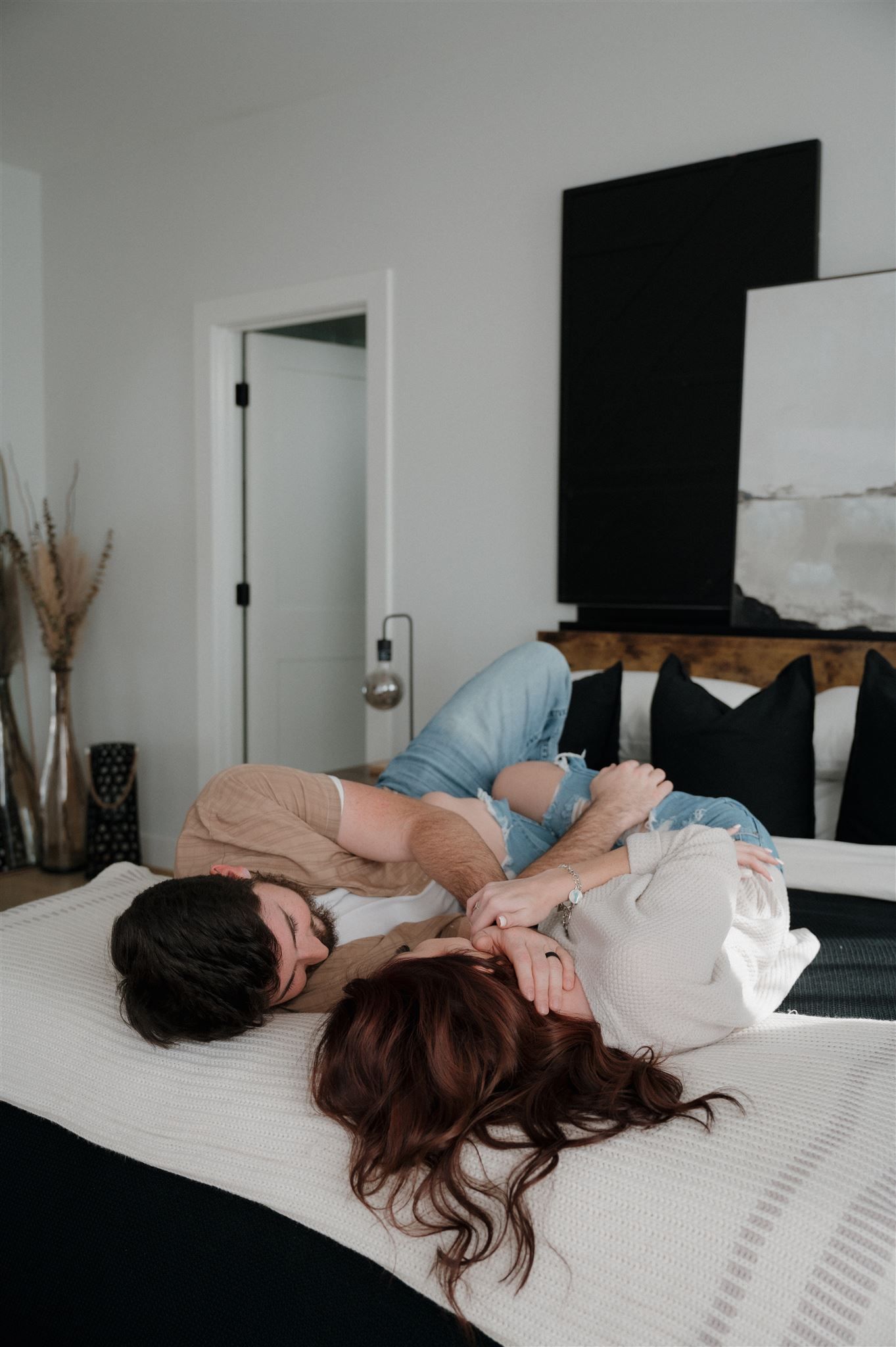 Two people lying on white bed in modern minimalist bedroom with black accents.