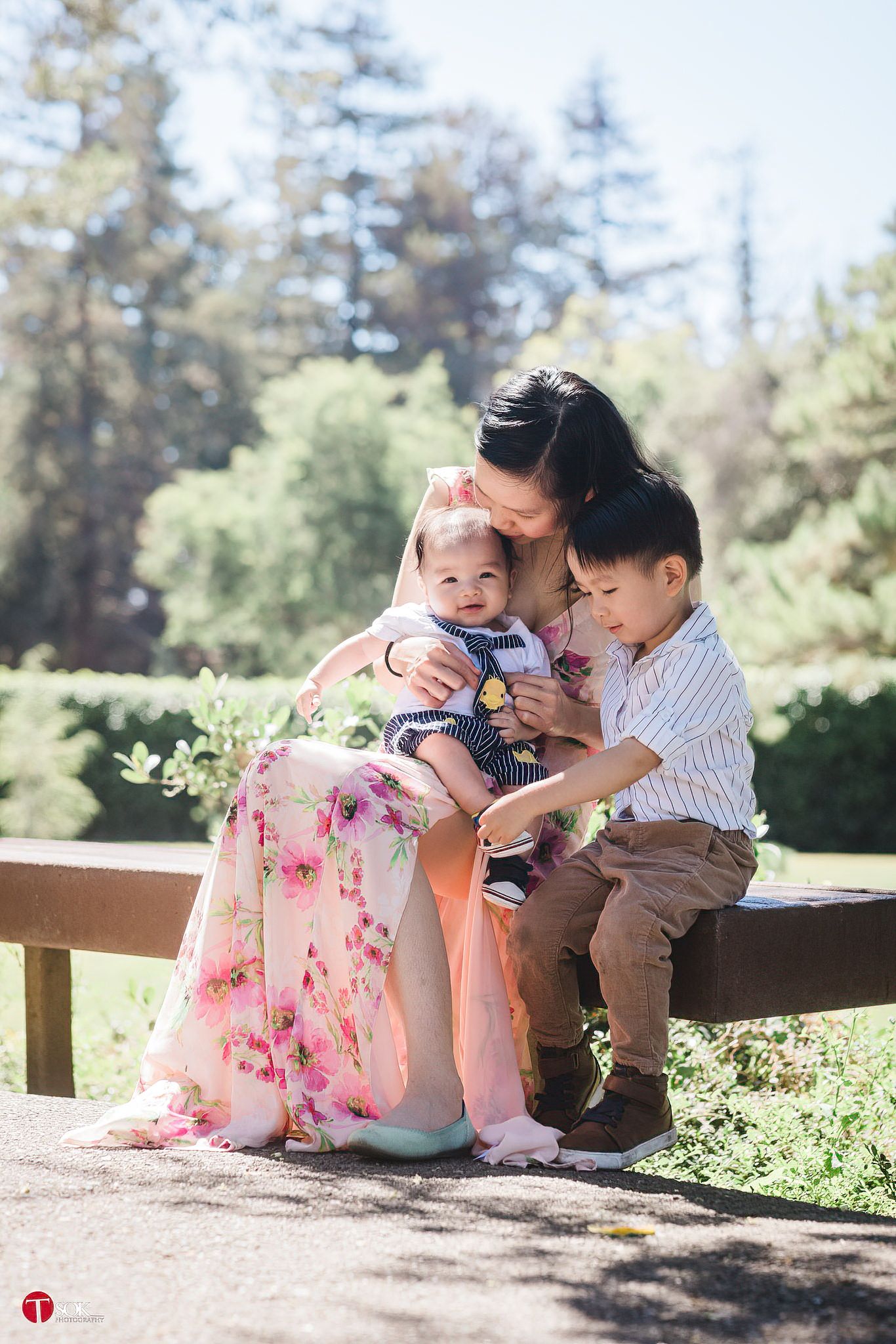 Three people share an intimate moment while sitting on a bench in a lush garden setting.