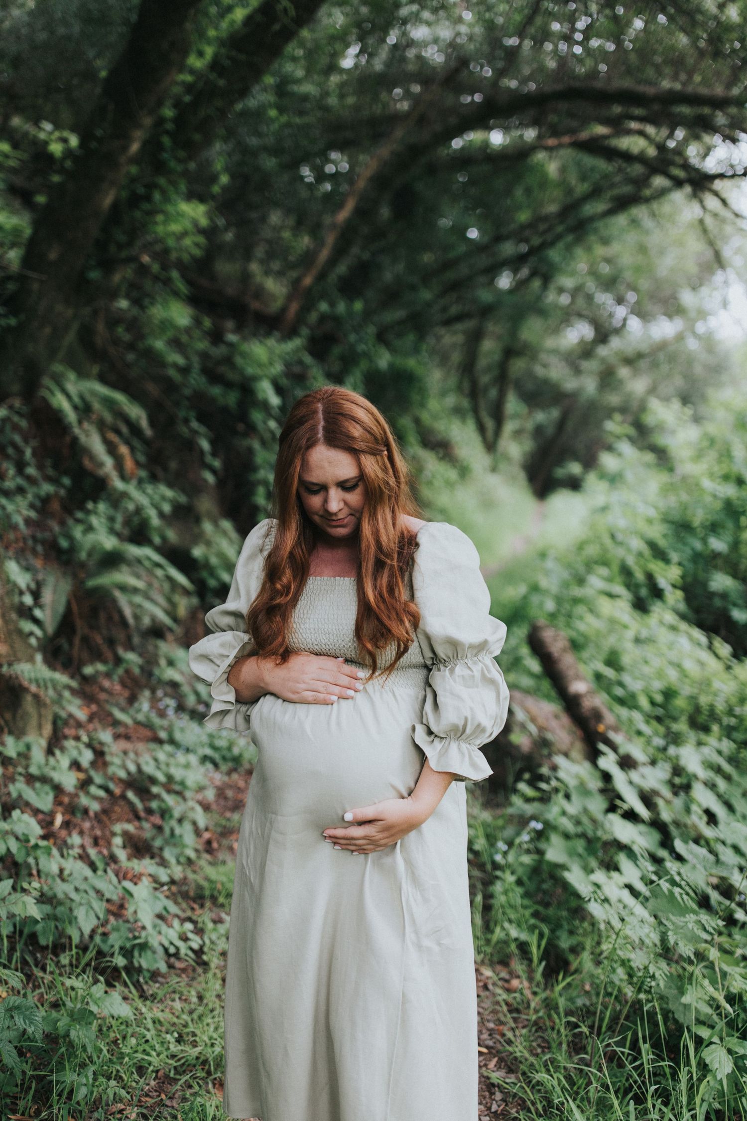 A serene maternity portrait in a white dress amidst lush greenery.