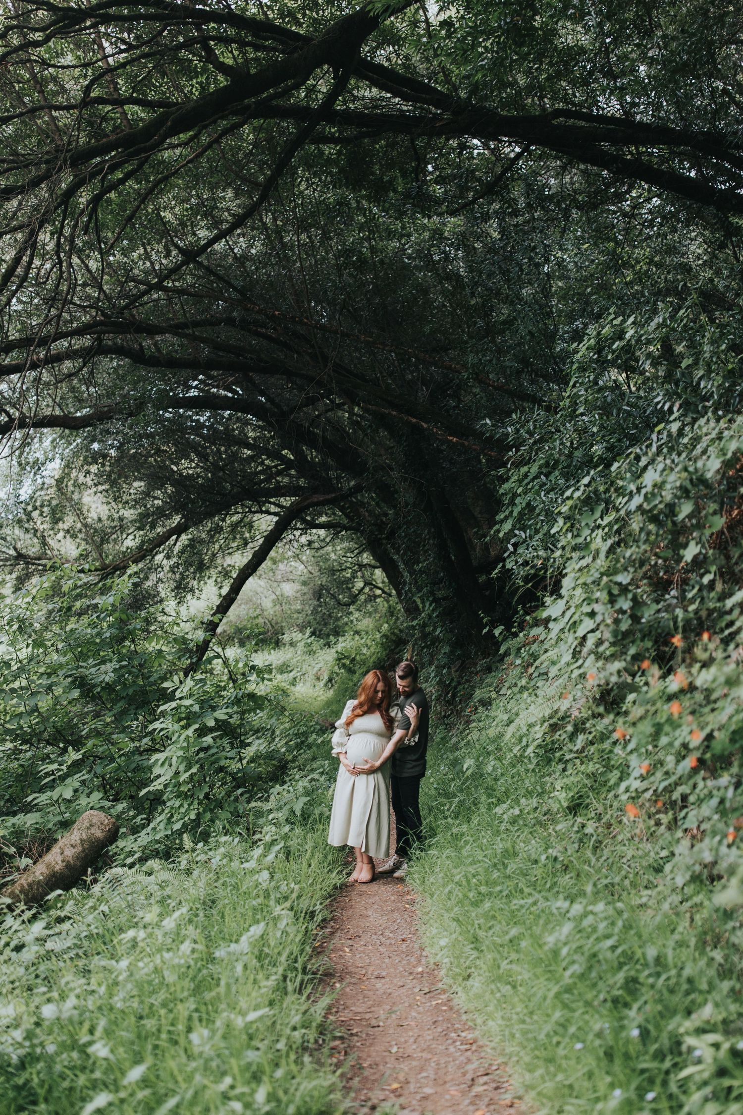 A romantic maternity photo beneath arching tree branches on a nature trail.