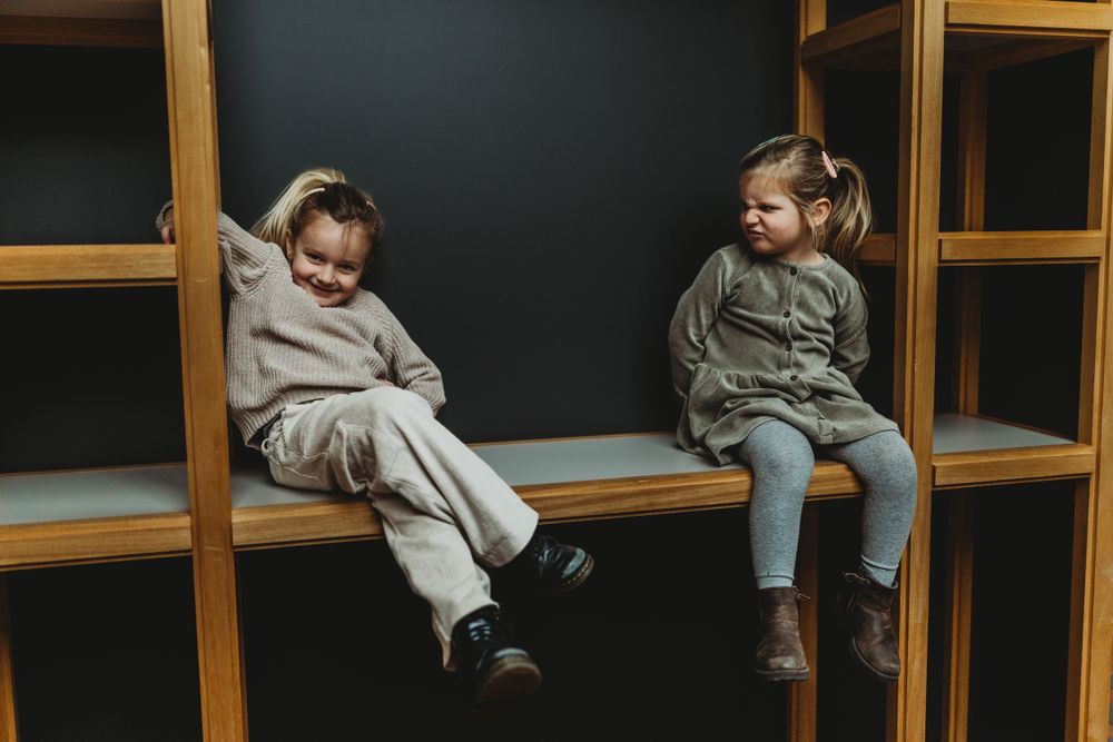 Two children sitting on wooden shelves in casual outfits.