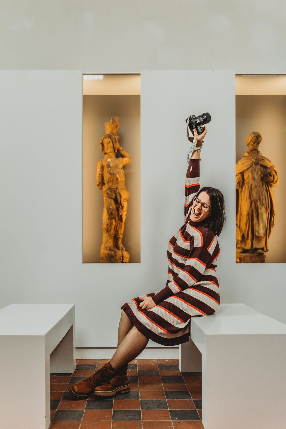 Playful pose in striped dress next to illuminated classical statues in museum setting.